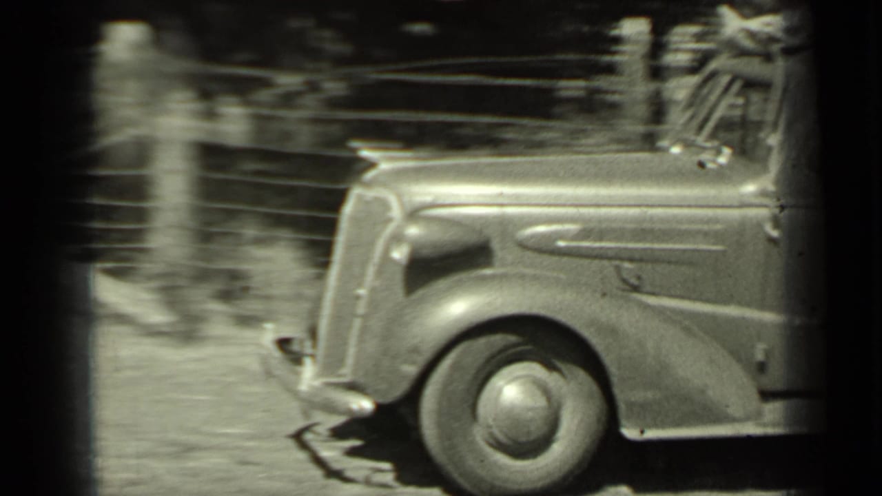 Classic car passing a roadside area with a dark vertical film edge.