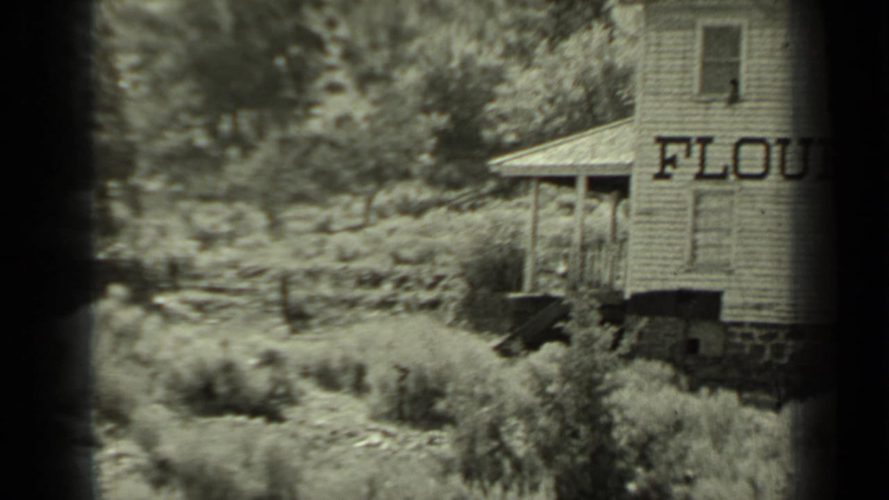 Wooden flour mill building partly framed by brush and dark film edges.