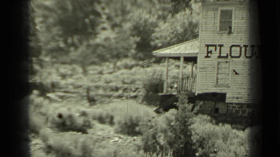 Home-movie still from Klamath, California showing the side of a rural wooden flour mill surrounded by vegetation.