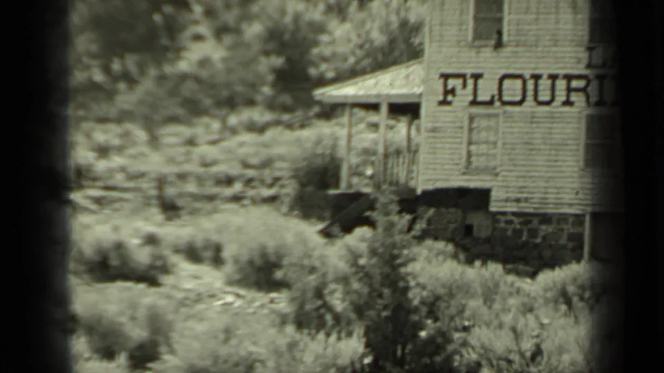 Klamath, California home-movie frame showing the mill's side wall, large FLOUR sign, small porch, and dense rural vegetation.