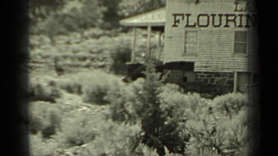 In Klamath, California, 1937, two figures move through dry brush near a weathered wooden building with partial "FLOURING" lettering.