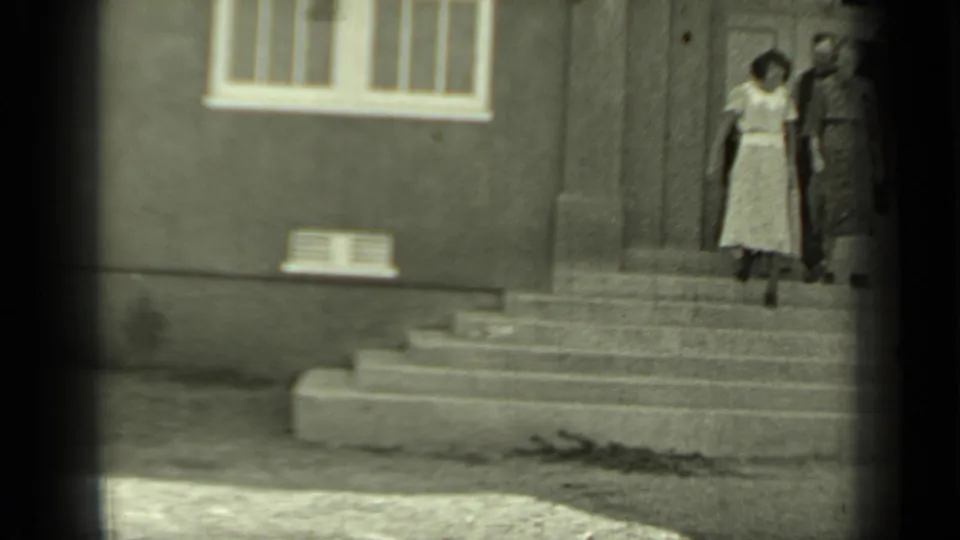 Two women in 1930s-style dress appear near stone steps outside a building in the Klamath, California archival home movie.