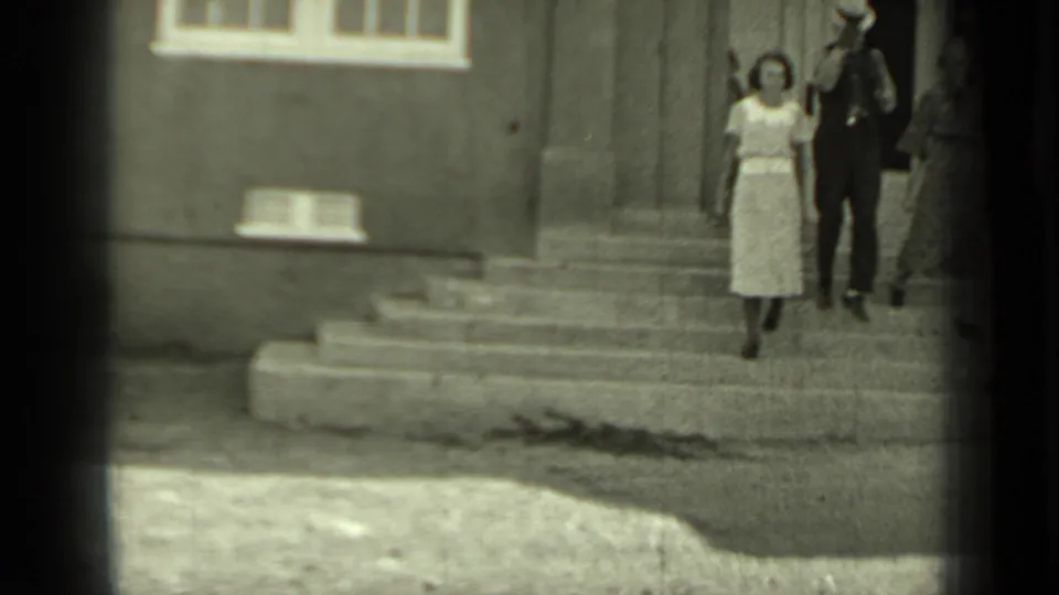 Two women and a hat-wearing man descend the exterior steps of a building in the 1937 Klamath, California clip.