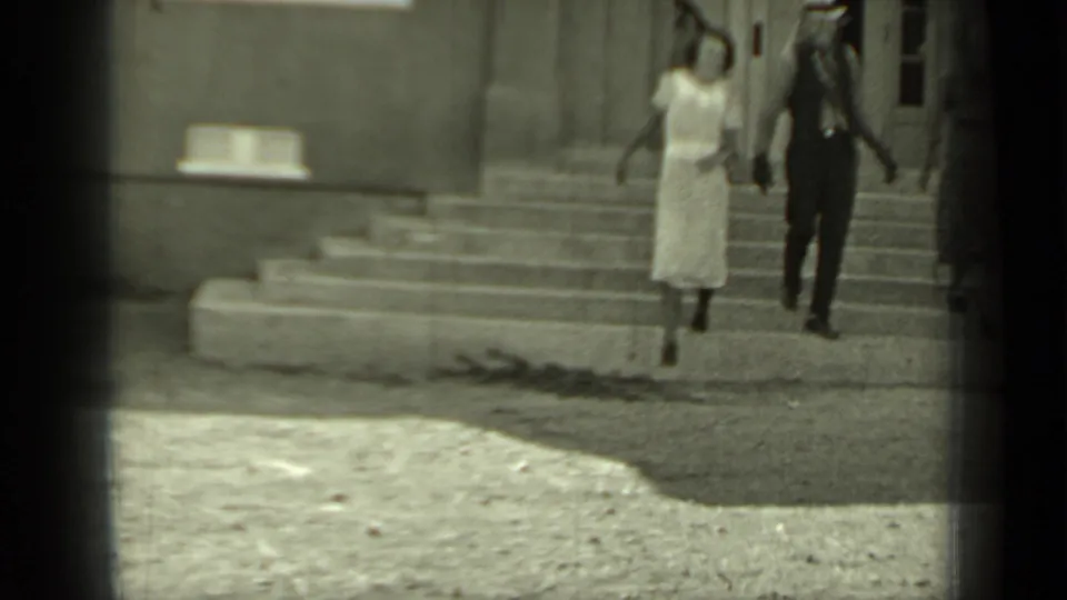 In Klamath, California, 1937, a man in a fedora and vest walks beside a woman in a light dress down stone steps.