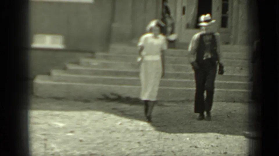 The same pair walks forward from the building steps in 1937 Klamath, with the woman in a light dress and the man in a hat.