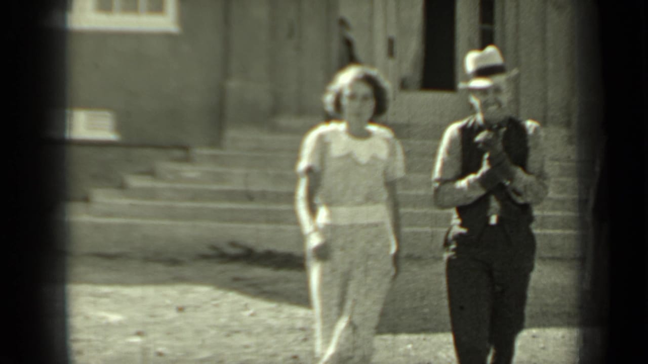 Woman in a light dress and man in a fedora walk down steps outside a building.
