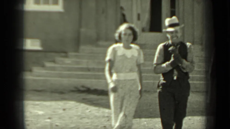 In 1937 Klamath, California footage, a woman in a light dress and a man with a camera approach from stone steps outside a building.
