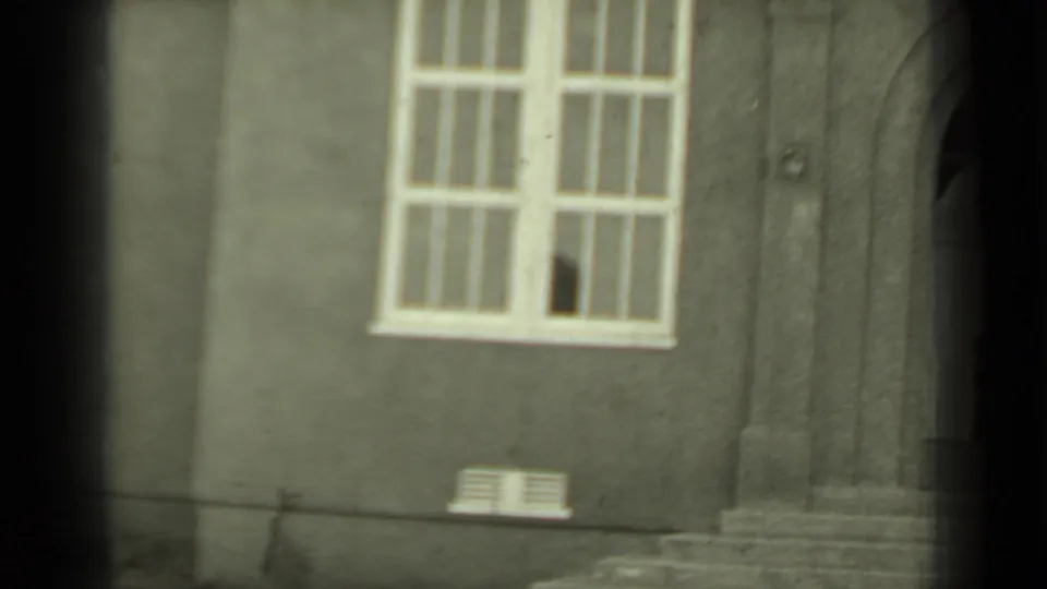 The final frame settles on the building exterior, showing a tall window with a broken pane and stone steps along the right edge.