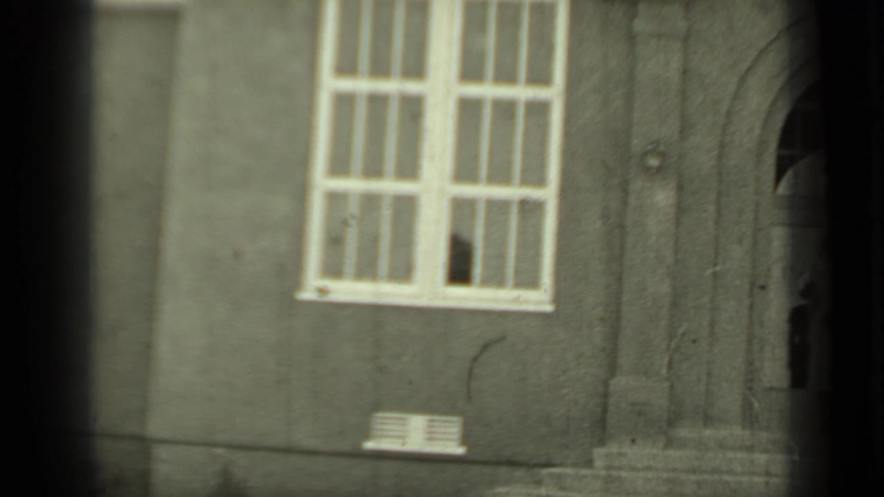Stucco building facade with a large multi-pane window and an arched doorway at the right edge.
