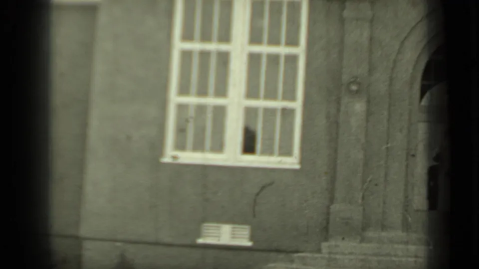 1937 Klamath, California home-movie frame showing a stucco wall, tall multi-pane window, and partial arched entryway.