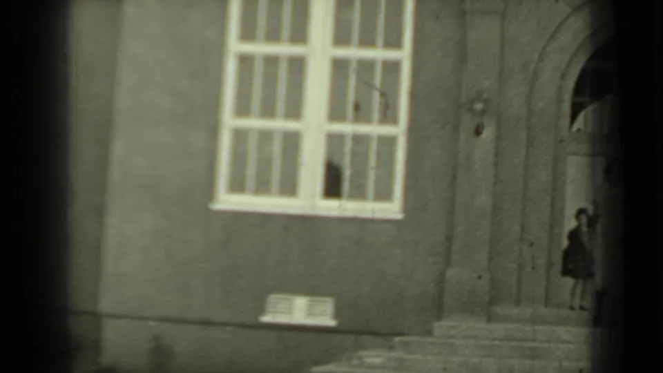 1937 Klamath, California frame with a person near a recessed arched doorway on a stucco building facade.