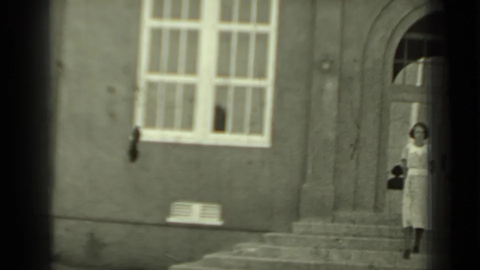 1937 Klamath, California frame showing a woman in a light dress on stone steps by a stucco building entrance.
