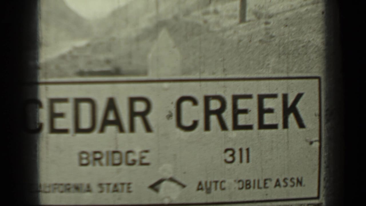 Close view of a Cedar Creek Bridge roadside sign with partial association wording below.