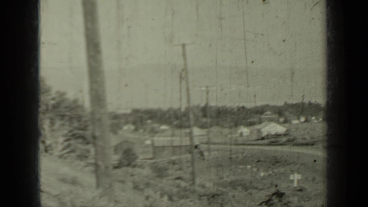 Rural road view with utility poles, small buildings, open fields, and dark film gate edges.