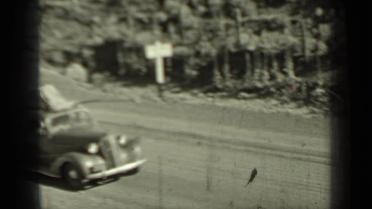 1937 Klamath-area home-movie frame showing a vintage car on a sunlit rural road, with soft focus and dark 8mm frame edges.
