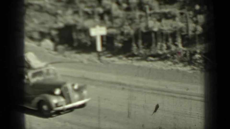 1937 Klamath-area home-movie frame showing a vintage car on a sunlit rural road, with soft focus and dark 8mm frame edges.