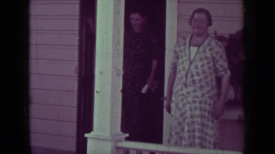 1937 Medford, Oregon home-movie frame showing adult women in dresses standing casually on a porch by a doorway.