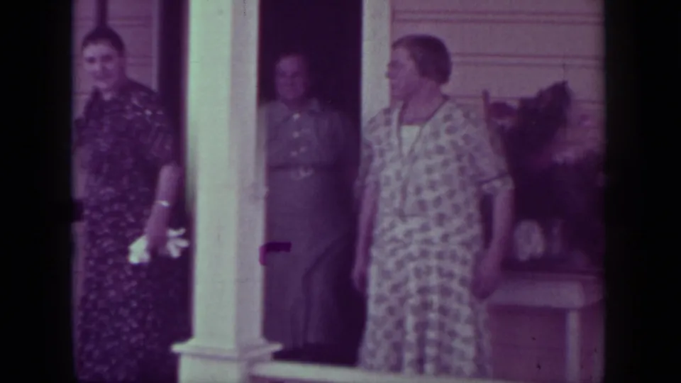 1937 Medford, Oregon frame showing three adult women on a porch, with a patterned dress, darker dresses, and house siding visible.