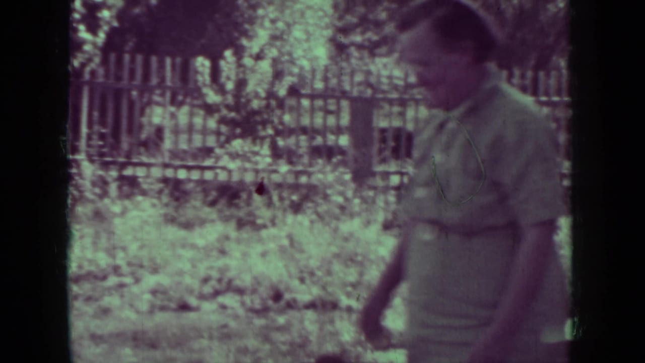 Older man walking beside a fence and garden plants outdoors.