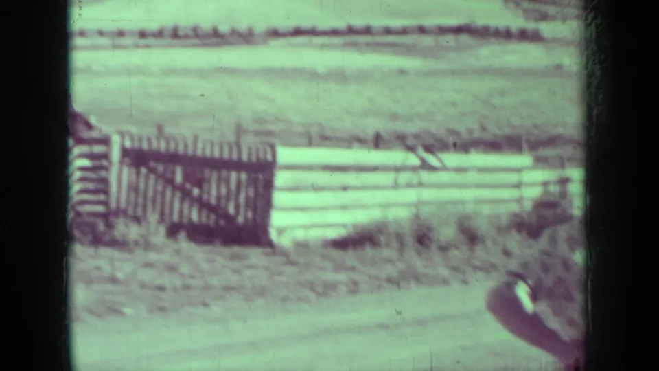 Medford, Oregon home-movie frame showing a wooden gate or fence beside open land, with part of a person entering at the right edge.