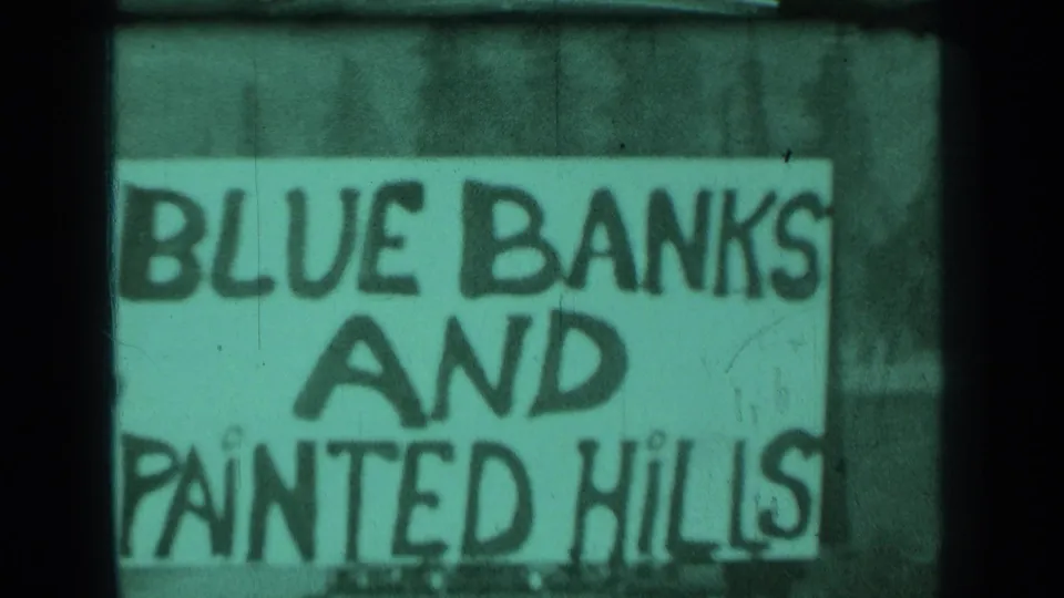 The same hand-lettered scenic sign appears in a green-tinted 8mm frame, with dark gate edges and visible film wear.