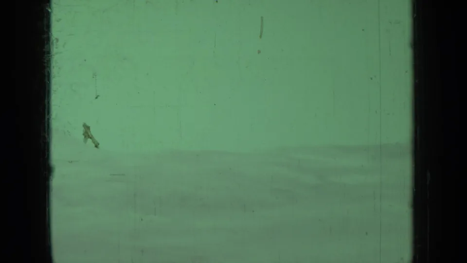 Green-tinted 8mm view of a muted sky over soft rolling hills, with scratches and dust visible in the film frame.