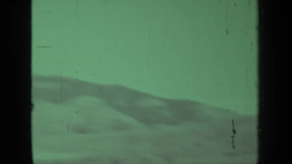 Archival 8mm landscape frame showing distant rolling hills under a muted sky, with green cast, scratches, and dark gate edge.