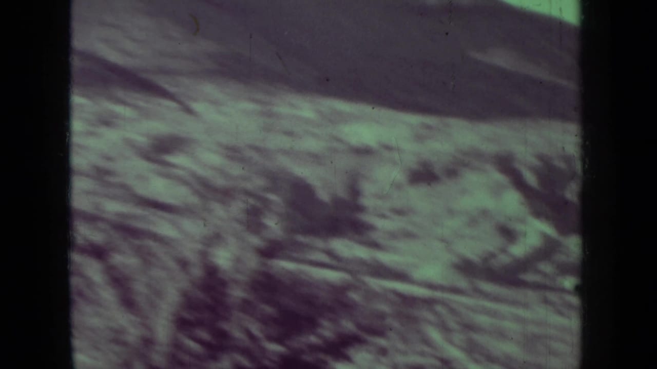 Blurred hillside and scrub terrain with a dark film border at the left.
