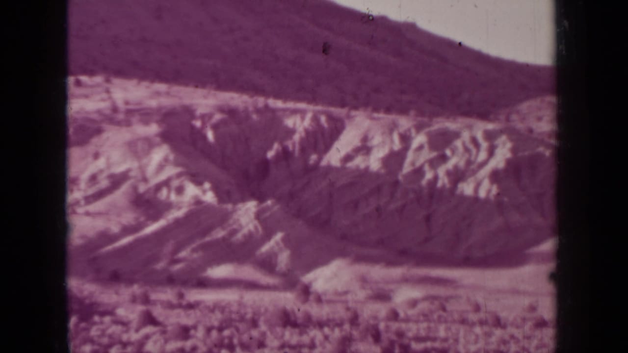 1937 Medford, Oregon home-movie frame showing pale eroded hills, darker mountain ridges, and a hazy sky with visible film borders.