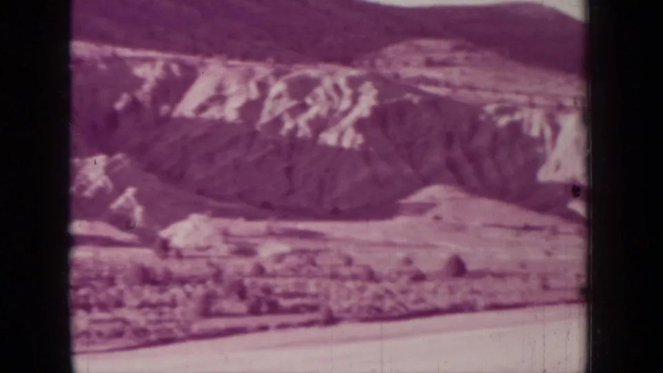 1937 Medford, Oregon landscape frame with layered rock formations, open terrain, and dark mountain ridges softened by film grain and color fading.