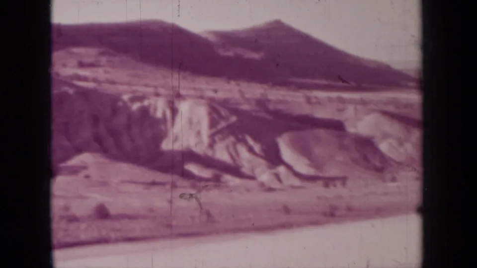 1937 Medford, Oregon home-movie still with a dark sloping ridge, pale eroded formations, and open ground framed by visible 8mm scan edges.