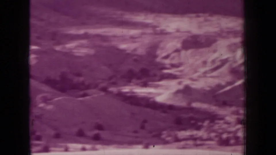 1937 8mm frame near Medford, Oregon, showing rugged slopes, pale cliff forms, and sparse dry terrain under a hazy sky.