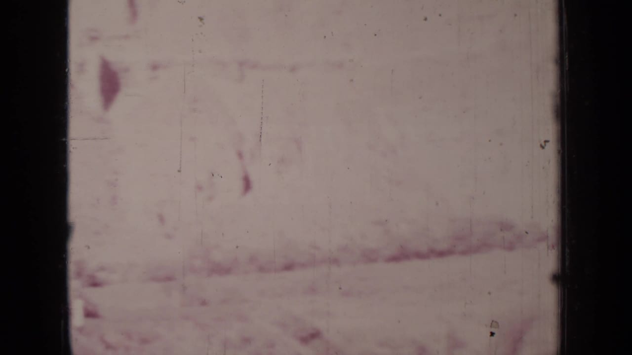 Faded pink frame with indistinct hillside or ground texture and dark film edges.