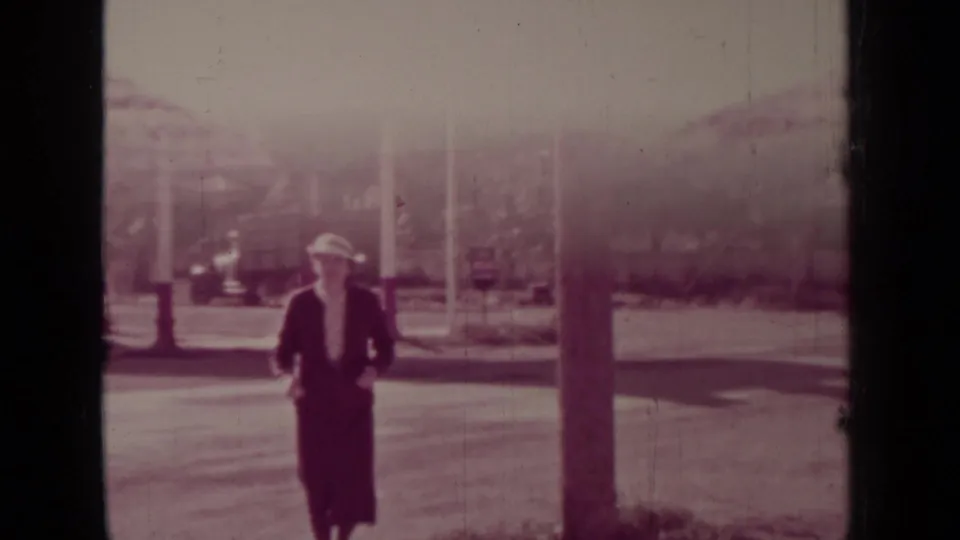 In the 1937 Medford, Oregon home-movie clip, a woman in a hat walks near a street-side gas station with columns and signage visible.