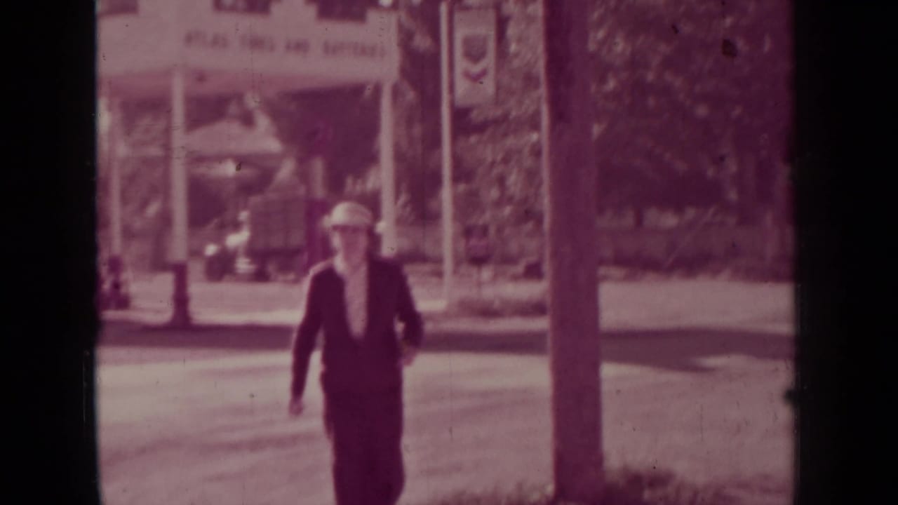 In Medford, Oregon, a woman in a 1930s-style suit and hat walks across the street toward the camera.