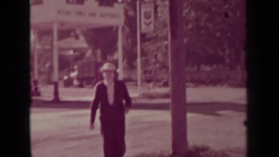 In Medford, Oregon, a woman in a 1930s-style suit and hat walks across the street toward the camera.