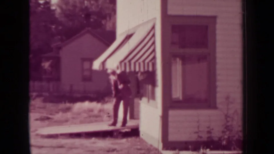In 1937 Medford, Oregon, a suited man stands by a striped storefront awning with a modest house and yard behind him.