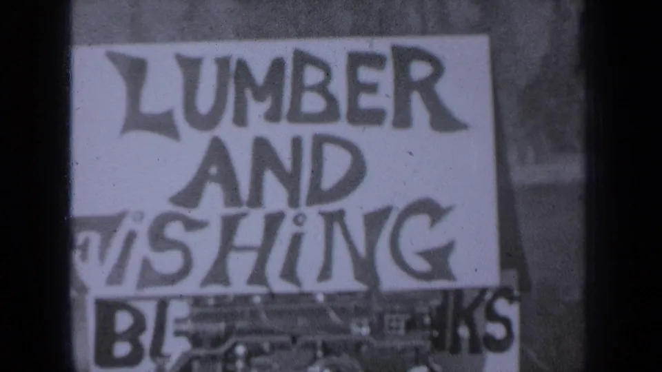 Medford, Oregon 8mm frame showing a bold hand-lettered sign with visible words including LUMBER, AND, FISHING, and BLANKS.