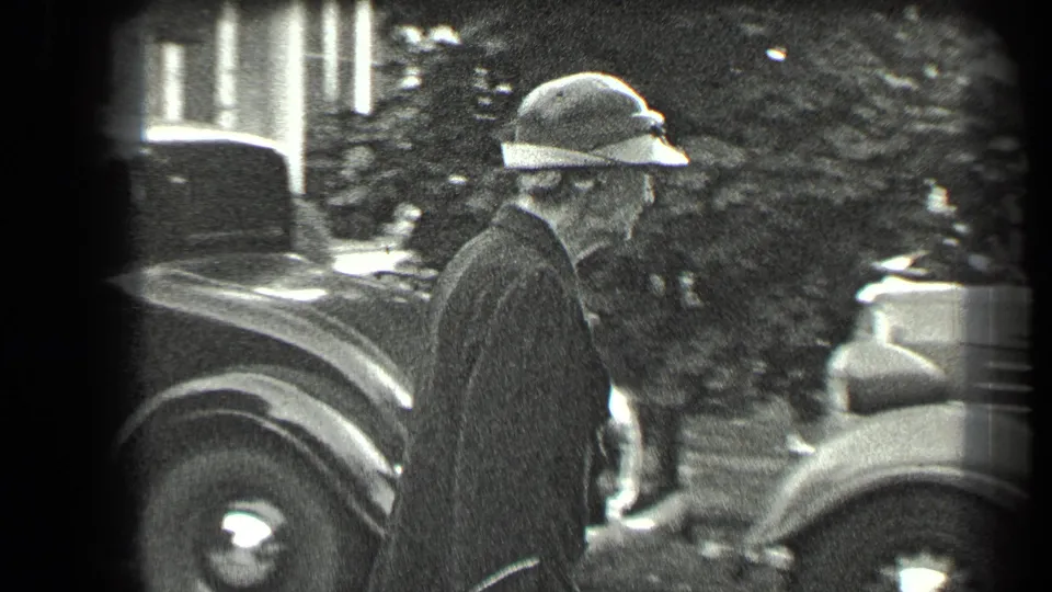 The woman walks beside a vintage car in an outdoor residential setting in Long Lake, Canada, 1939.