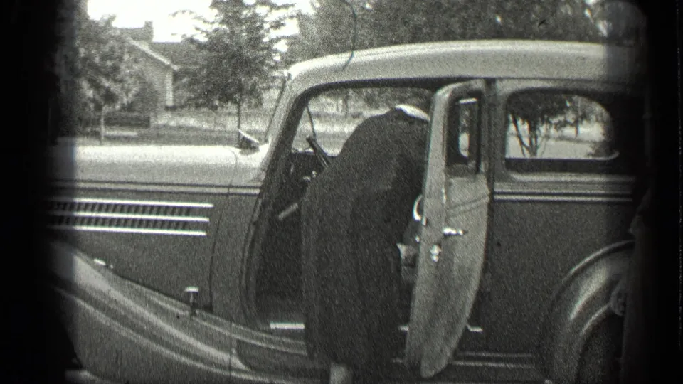 The woman leans into the open door of the grey vintage car in the 1939 Long Lake home-movie scene.