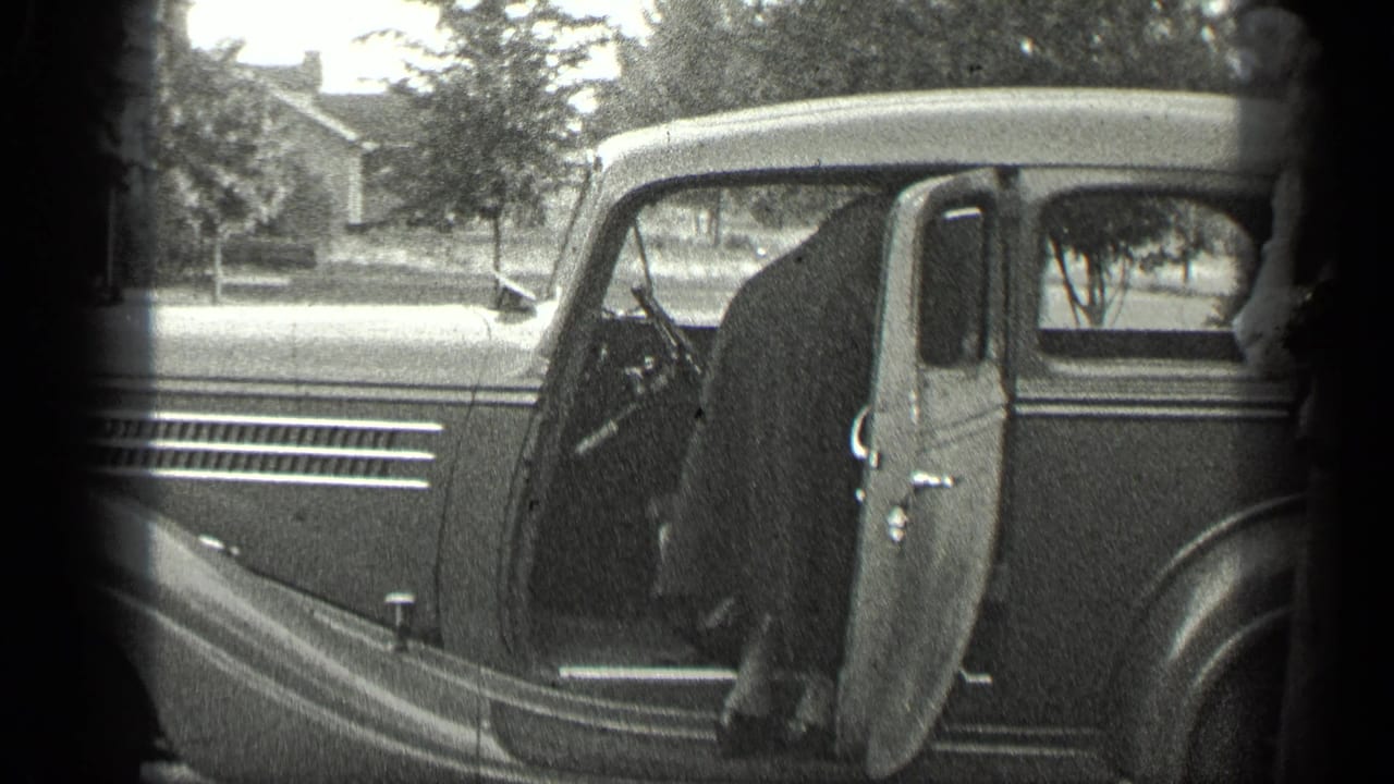 Parked vintage car with an open door beside trees and a house exterior.