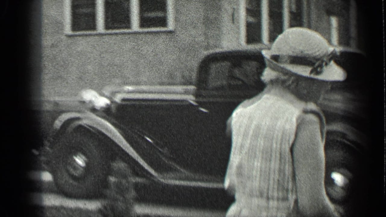 Woman in a hat seen from behind beside a dark classic car and house windows.