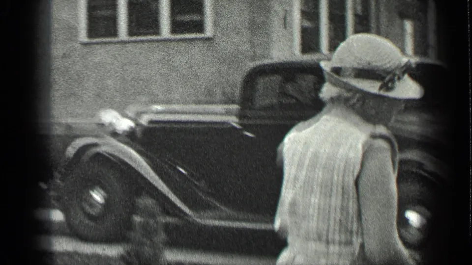 In Long Lake, Canada, a woman in a wide-brimmed hat and patterned dress stands near a classic car in 1939 home-movie footage.