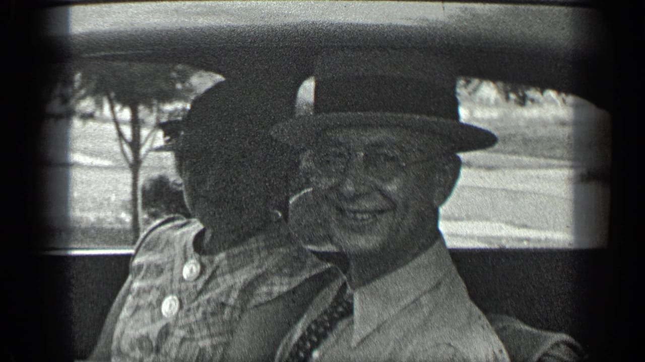 Older man in a fedora and glasses smiles beside a woman inside a car.