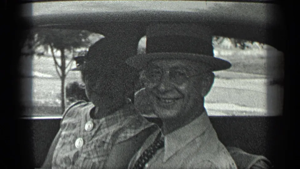 In 1939 Long Lake, Canada footage, an older man in a fedora and glasses smiles beside a woman in a patterned dress inside a car.