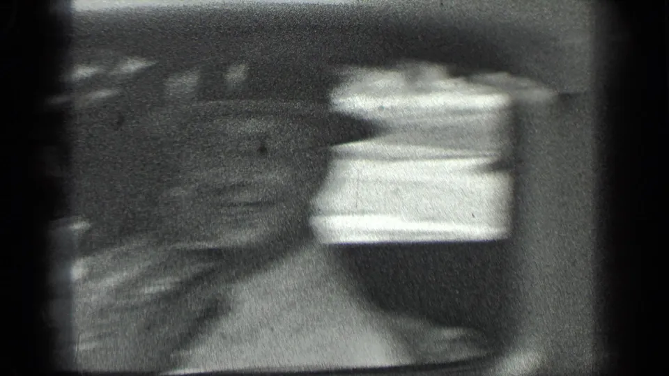 A blurred 8mm frame shows indistinct passengers and a bright car window during handheld movement in the Long Lake car scene.