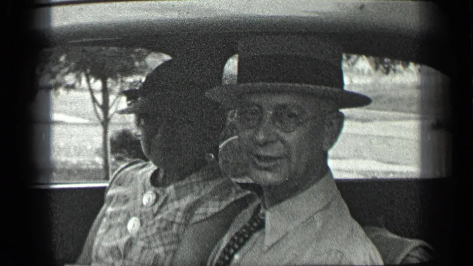 In 1939 home-movie footage from Long Lake, Canada, a man in a fedora smiles from a car seat beside a woman.