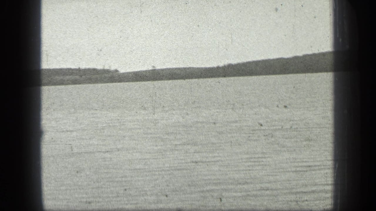 1939 8mm home-movie frame of Long Lake, Canada, showing rippled water, a low far shore, pale sky, and dark gate borders.
