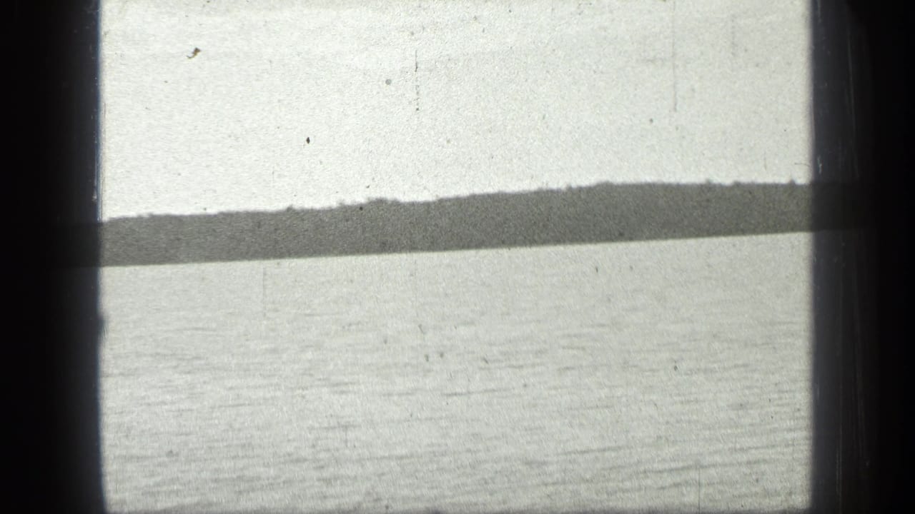 Lake horizon seen through dark 8mm frame edges with pale water and distant wooded shore.