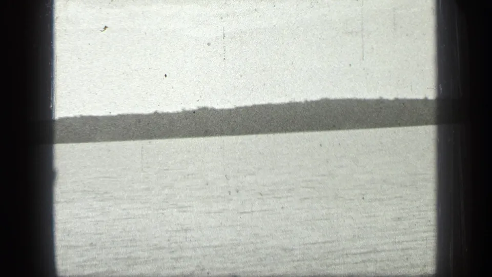 1939 Long Lake, Canada home-movie frame showing pale lake water, distant shore, and heavy film-frame shadows.